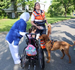 Rettungshund mit Frauchen bei Patientinn am Rollstuhl. Pflegerin steht der Patientin bei