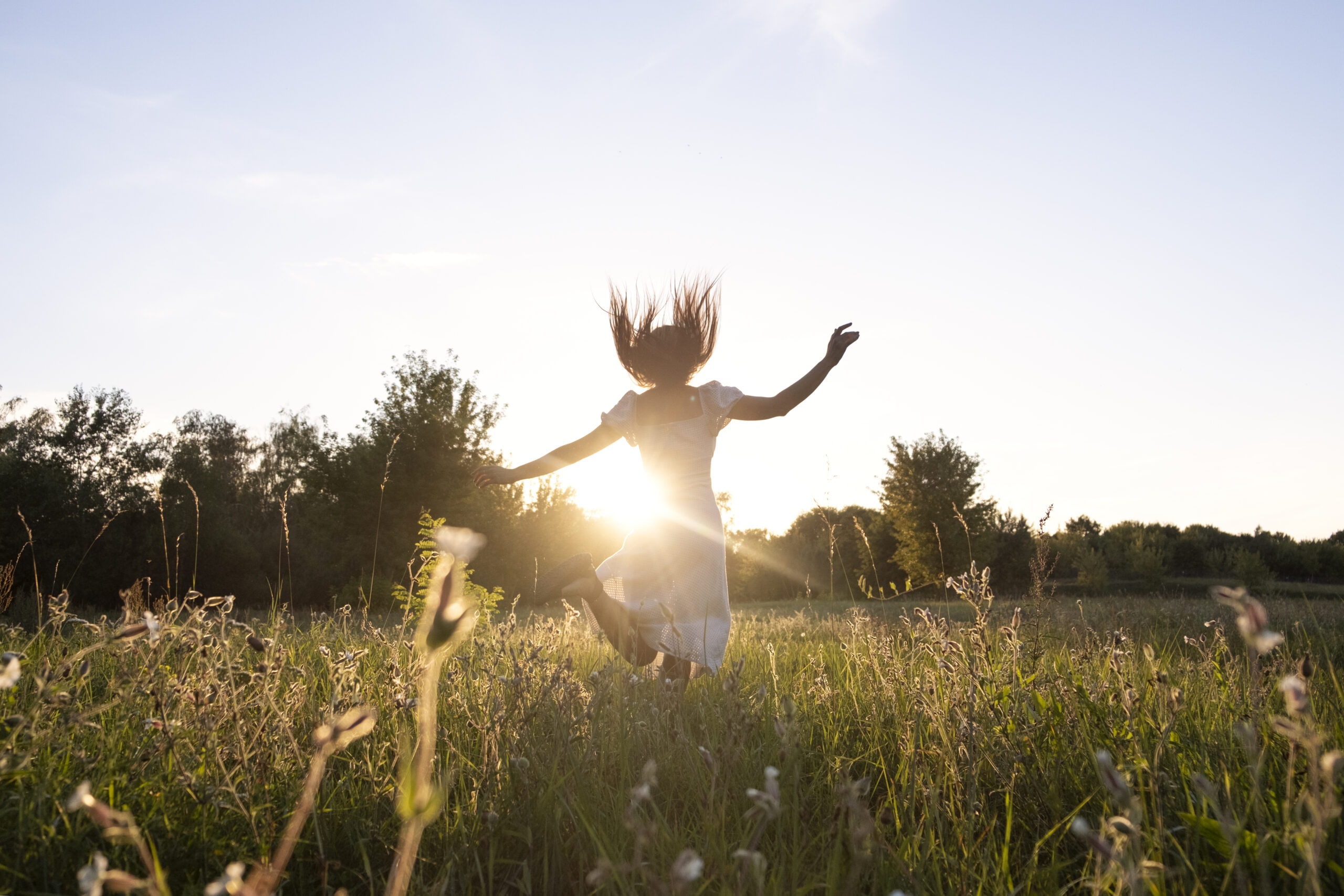 Frau springt bei strahlender Sonne im Blumenfeld